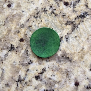 Peut inclure: Un objet rond vert fonc&eacute; avec une surface textur&eacute;e. L'objet est centr&eacute; dans l'image et semble &ecirc;tre en cuir ou dans un mat&eacute;riau similaire. L'arri&egrave;re-plan est une surface tachet&eacute;e de couleur claire.