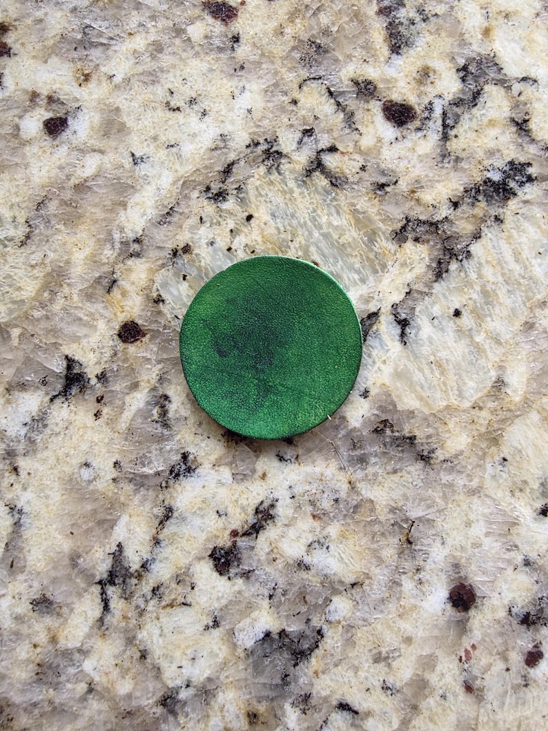 Peut inclure: Un objet rond vert fonc&eacute; avec une surface textur&eacute;e. L'objet est centr&eacute; dans l'image et semble &ecirc;tre en cuir ou dans un mat&eacute;riau similaire. L'arri&egrave;re-plan est une surface tachet&eacute;e de couleur claire.