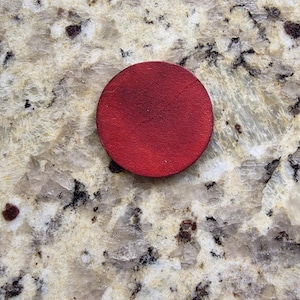 Peut inclure: Un dessous de verre rond en cuir rouge. Le dessous de verre est d'un rouge profond et semble &ecirc;tre fait d'une seule pi&egrave;ce de cuir. Le dessous de verre est circulaire et a une surface lisse.
