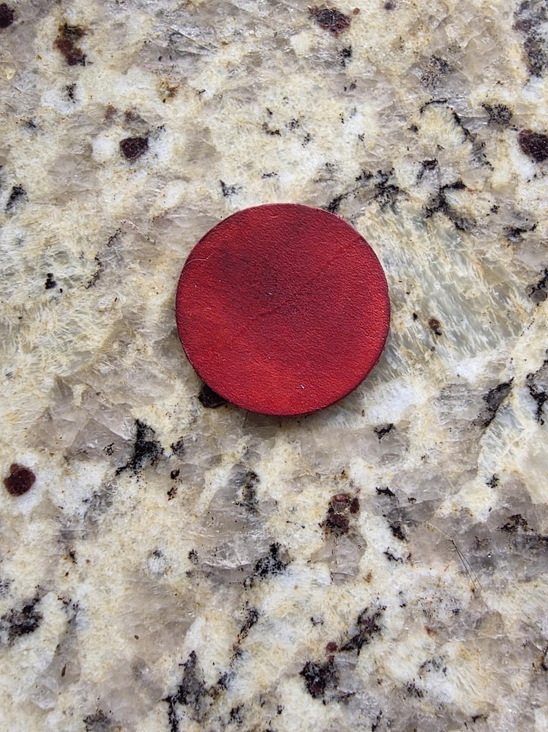 Peut inclure: Un dessous de verre rond en cuir rouge. Le dessous de verre est d'un rouge profond et semble &ecirc;tre fait d'une seule pi&egrave;ce de cuir. Le dessous de verre est circulaire et a une surface lisse.