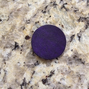 Peut inclure: Un objet rond, violet fonc&eacute;, avec une surface textur&eacute;e. L'objet est centr&eacute; dans le cadre et semble &ecirc;tre fait d'un mat&eacute;riau solide. Le fond est une surface claire et mouchet&eacute;e.