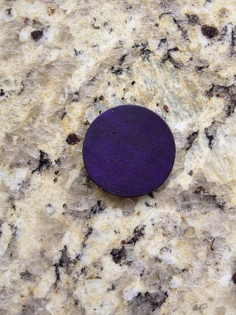 Peut inclure: Un objet rond, violet fonc&eacute;, avec une surface textur&eacute;e. L'objet est centr&eacute; dans le cadre et semble &ecirc;tre fait d'un mat&eacute;riau solide. Le fond est une surface claire et mouchet&eacute;e.