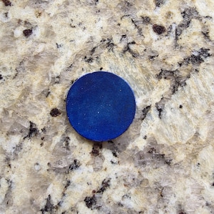 Peut inclure: Un objet rond bleu fonc&eacute;. L'objet est un cercle plat avec une surface lisse. Le fond est une surface tachet&eacute;e de couleur claire avec des mouchetures marron fonc&eacute; et noires.