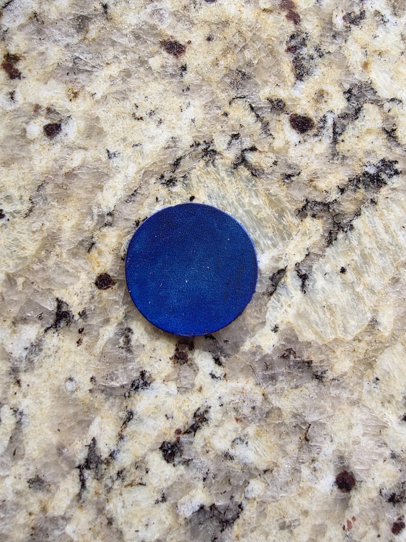 Peut inclure: Un objet rond bleu fonc&eacute;. L'objet est un cercle plat avec une surface lisse. Le fond est une surface tachet&eacute;e de couleur claire avec des mouchetures marron fonc&eacute; et noires.