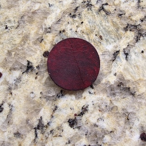 Peut inclure: Un dessous de verre rond en cuir bordeaux fonc&eacute;. Le dessous de verre est circulaire et pr&eacute;sente une surface textur&eacute;e. La couleur est une nuance profonde et riche de rouge-brun. Il est utilis&eacute; pour prot&eacute;ger les surfaces des boissons.