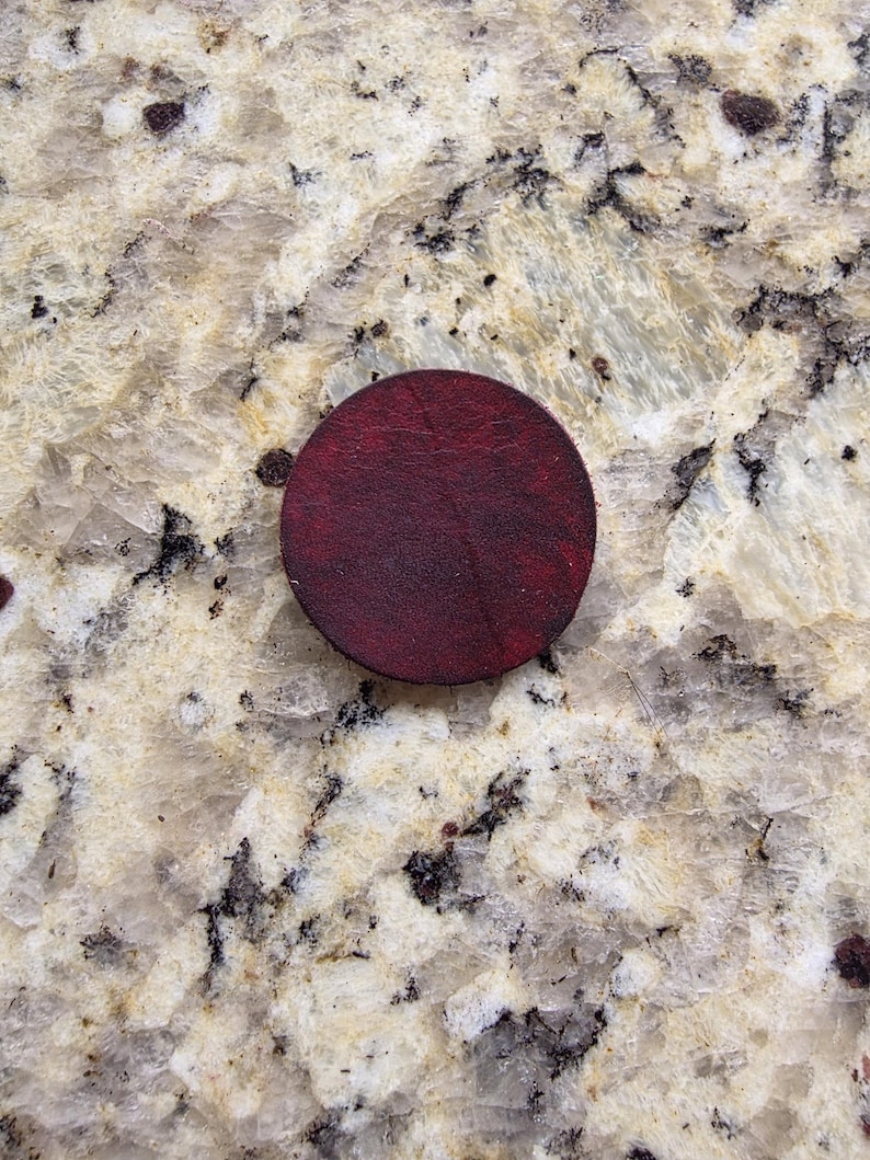 Peut inclure: Un dessous de verre rond en cuir bordeaux fonc&eacute;. Le dessous de verre est circulaire et pr&eacute;sente une surface textur&eacute;e. La couleur est une nuance profonde et riche de rouge-brun. Il est utilis&eacute; pour prot&eacute;ger les surfaces des boissons.