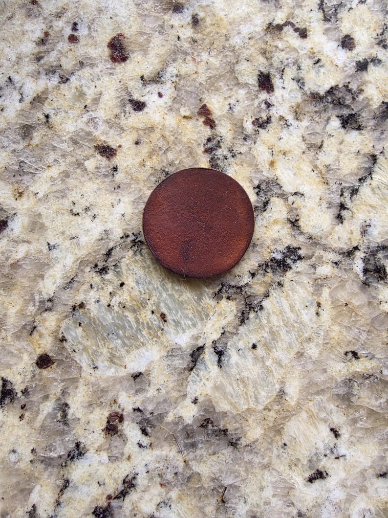 Peut inclure: Un petit objet rond, brun fonc&eacute;, possiblement un bouton en bois ou un &eacute;l&eacute;ment d&eacute;coratif, repose sur une surface tachet&eacute;e de couleur claire. La couleur de l'objet contraste avec l'arri&egrave;re-plan, soulignant sa forme et sa texture. L'image est un gros plan.