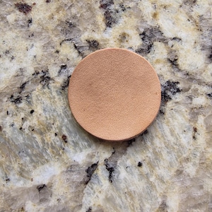 Peut inclure: Un dessous de verre rond en cuir brun clair. Le dessous de verre est de couleur unie et a une surface lisse. Il est con&ccedil;u pour prot&eacute;ger les surfaces de la condensation des boissons. Diam&egrave;tre d'environ 8 cm.