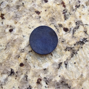 Peut inclure: Un dessous de verre circulaire en cuir bleu fonc&eacute;. Le dessous de verre est de couleur unie et semble &ecirc;tre fait d'un mat&eacute;riau en cuir textur&eacute;. Le dessous de verre est pos&eacute; sur une surface claire et mouchet&eacute;e.