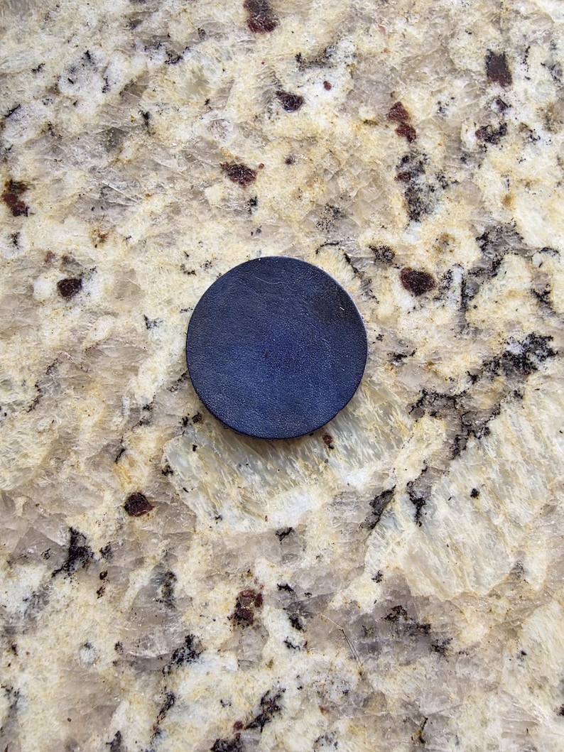Peut inclure: Un dessous de verre circulaire en cuir bleu fonc&eacute;. Le dessous de verre est de couleur unie et semble &ecirc;tre fait d'un mat&eacute;riau en cuir textur&eacute;. Le dessous de verre est pos&eacute; sur une surface claire et mouchet&eacute;e.