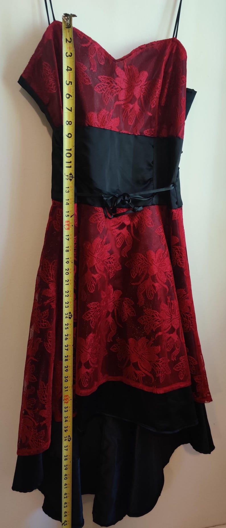 May include: A formal dress featuring a red floral lace overlay. The dress has a black satin waistband and a layered skirt. The total length of the dress is approximately 44 inches.