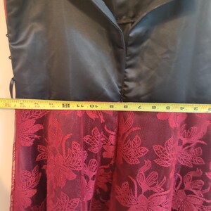 May include: A black satin dress bodice with a zipper closure, transitioning to a burgundy floral lace skirt. The dress is measured with a yellow tape measure. The skirt has a floral pattern.