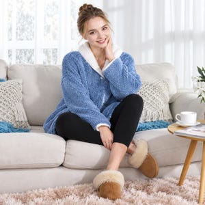 May include: A blue fleece jacket with a white collar, black leggings, and tan slip-on slippers with a cream-colored faux fur lining. The jacket features a textured, fuzzy material and a button-down front, providing a soft and cozy appearance.