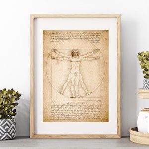 May include: A framed print of Leonardo da Vinci's Vitruvian Man. The artwork features a detailed sketch of a nude male figure within a circle and square, with handwritten notes. The frame is light wood, and the print has a sepia tone.