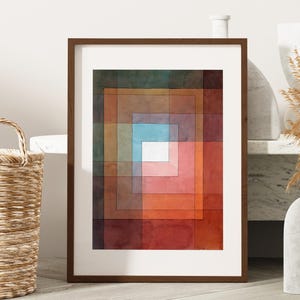 Op de afbeelding: Ingelijste abstracte kunstprint met een reeks geneste vierkanten in tinten rood, oranje, bruin, groen en blauw. Het kunstwerk zit in een bruine houten lijst met een witte passe-partout. Thema: interieurdecoratie.