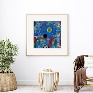 May include: Abstract art print in a wooden frame. The artwork features a blue background with colourful shapes, including a black circle, a yellow circle, and red and green plant-like forms. The print is displayed in a bright room with a plant and a chair.