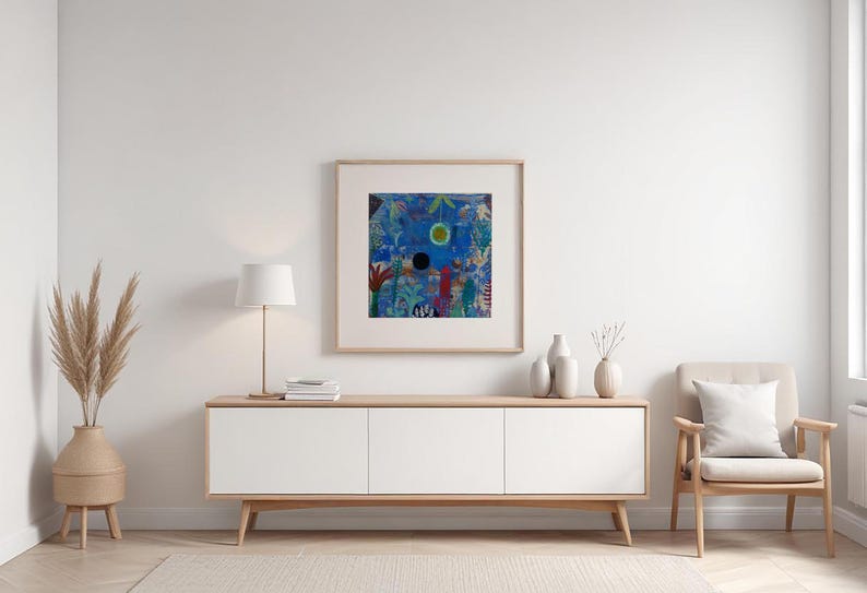May include: An abstract painting in a wooden frame hangs above a white cabinet. The artwork features a blue background with colourful shapes and a central black circle. A beige chair and decorative vases complete the scene.