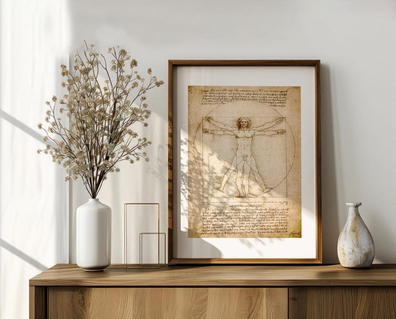 May include: A framed print of Leonardo da Vinci's Vitruvian Man, displayed on a wooden cabinet. The artwork features a detailed sketch of a man within a circle and square, with handwritten notes. A white vase with dried flowers and a decorative vase are also on the cabinet.