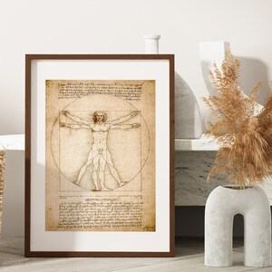 May include: A framed print of Leonardo da Vinci's Vitruvian Man, featuring a male figure within a circle and square, with detailed anatomical drawings and handwritten text. The artwork is displayed in a brown frame with a white mat.