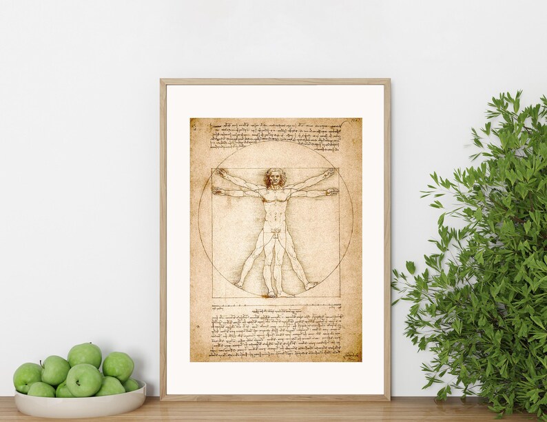 May include: Framed print of Leonardo da Vinci's Vitruvian Man. The artwork features a detailed pen and ink drawing of a nude male figure within a circle and a square, with handwritten text. The frame is a light wood color.