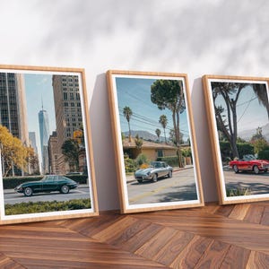 Op de afbeelding: Drie ingelijste prints met klassieke auto's in stedelijke en voorstedelijke omgevingen. De eerste print toont een groene cabriolet in een stad, de tweede een zilveren auto in een woonstraat en de derde een rode cabriolet.