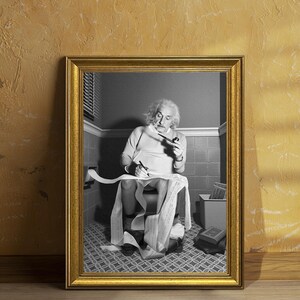 May include: A framed black and white photograph depicting a person with wild hair sitting on a toilet, holding a pipe in one hand and a pen in the other, writing on a long, continuous roll of paper that drapes over their lap and onto the floor.