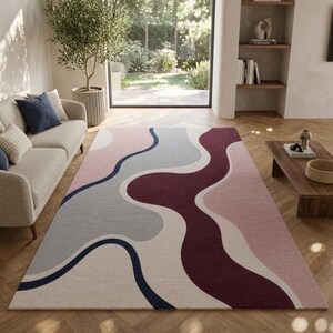 May include: A large area rug with an abstract design in shades of pink, gray, cream, and burgundy. The rug features flowing, wavy lines and is placed on a hardwood floor in a living room setting.