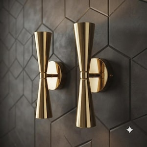 May include: Two wall-mounted light fixtures with a polished gold finish. Each fixture features a double-cone design with two symmetrical, tapered conical shades connected to a central circular base that attaches directly to the wall surface.