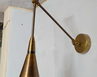 May include: A brass wall sconce with a conical shade and adjustable arm. The sconce features a circular base and a long, slender arm extending from the base to the shade. The shade is cone-shaped with small perforations near the bottom.