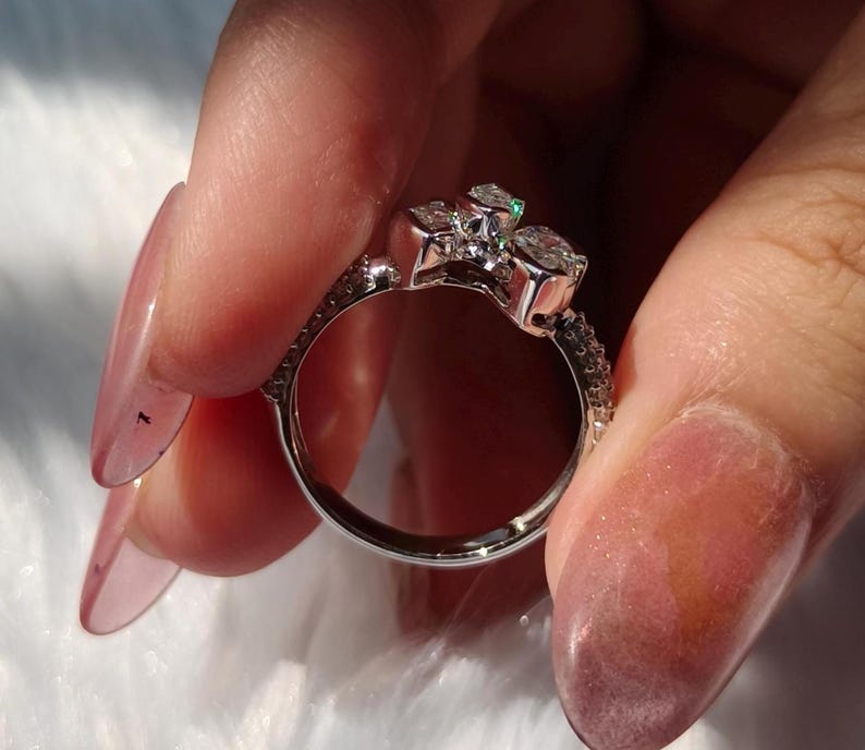 May include: A silver-toned ring featuring a cluster of three clear, faceted stones set at the top. The band is metallic and smooth on the interior, with a textured, pav&eacute;-style surface along the outer edges leading up to the central stone setting.