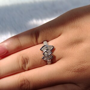 May include: A silver-toned ring featuring three marquise-cut stones arranged in a vertical cluster. The band is encrusted with small, pav&eacute;-set clear stones that extend along the shank, creating a textured, sparkling appearance on the metal surface.
