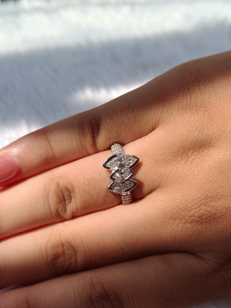 May include: A silver-toned ring featuring three marquise-cut stones arranged in a vertical cluster. The band is encrusted with small, pav&eacute;-set clear stones that extend along the shank, creating a textured, sparkling appearance on the metal surface.
