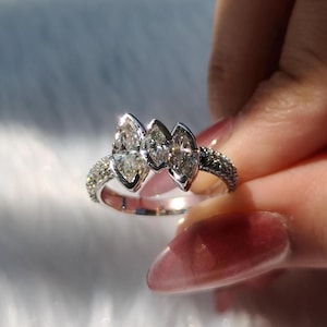 May include: A silver-toned ring featuring three prominent marquise-cut clear stones arranged horizontally in the center, flanked by a band encrusted with numerous small, sparkling pav&eacute;-set stones that extend along the sides of the metal band.
