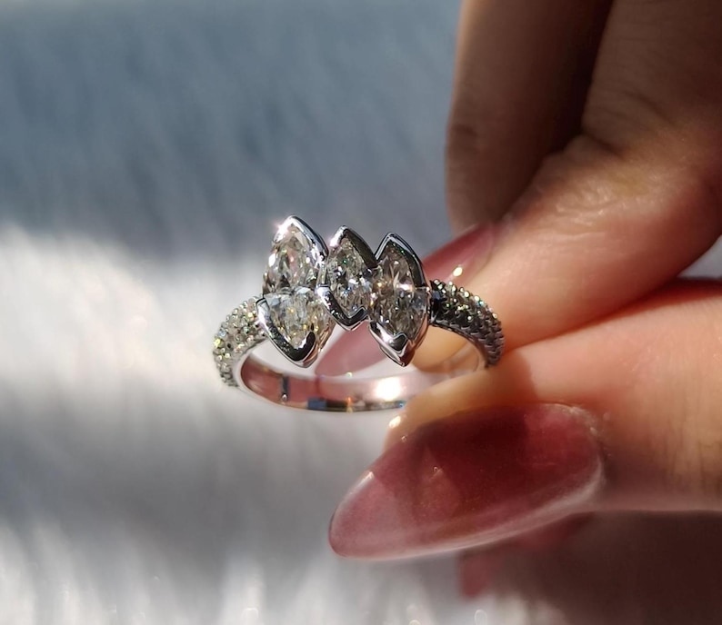 May include: A silver-toned ring featuring three prominent marquise-cut clear stones arranged horizontally in the center, flanked by a band encrusted with numerous small, sparkling pav&eacute;-set stones that extend along the sides of the metal band.