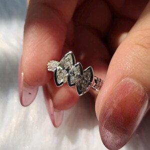 May include: A silver-toned ring featuring three marquise-cut stones arranged horizontally in a bezel setting. The band has a textured, grid-like pattern along the sides, providing a distinct contrast to the smooth, polished metal surrounding the stones.