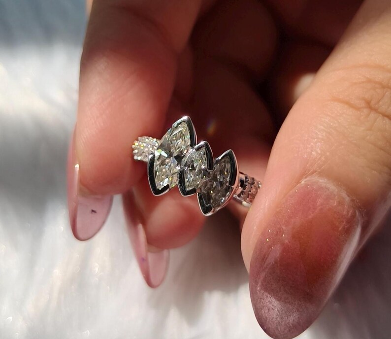 May include: A silver-toned ring featuring three marquise-cut stones arranged horizontally in a bezel setting. The band has a textured, grid-like pattern along the sides, providing a distinct contrast to the smooth, polished metal surrounding the stones.