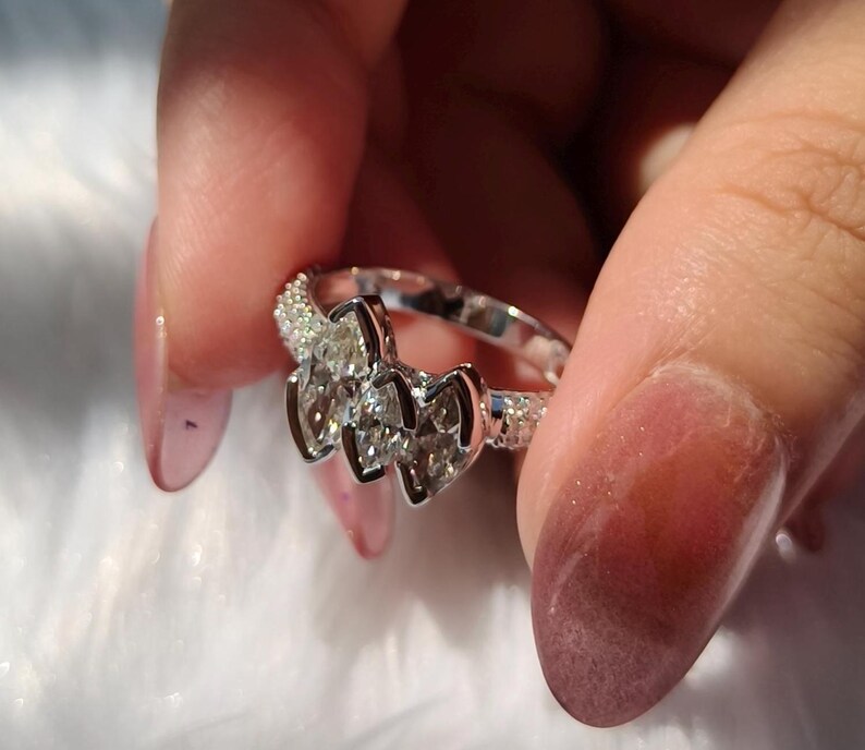 May include: A silver-toned ring featuring three prominent marquise-cut clear stones arranged horizontally in the center, flanked by bands encrusted with small, shimmering pav&eacute;-set stones along the sides of the metal shank.