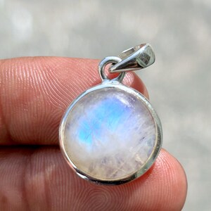 Op de afbeelding: Ronde zilveren hanger met een maansteen met een blauw-witte iriserende gloed. De maansteen is gezet in een gepolijste zilveren rand met een kleine lus voor een ketting.