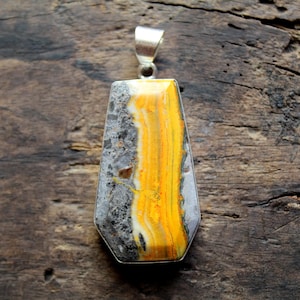 Op de afbeelding: Een rechthoekige hanger met een zilveren beugel. De hanger heeft een opvallend patroon van gele, grijze en witte steen, gezet in een zilveren rand. De steen heeft een uniek, natuurlijk patroon.