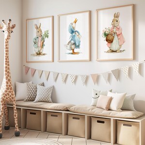 Könnte beinhalten: Drei gerahmte Aquarelldrucke von anthropomorphen Tieren: ein Hase mit einer Karotte, eine Ente mit einer Haube und ein Hase mit einem Blumenkorb. Ein Giraffenspielzeug und eine Bank mit Kissen und Aufbewahrungswürfeln vervollständigen die Kinderzimmerdekoration.