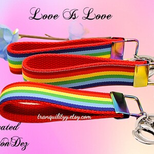 May include: A rainbow striped key chain with a silver key ring and the text "Love Is Love". The key chain is made of red, orange, yellow, green, blue, indigo, and violet striped fabric. The key chain is attached to a silver key ring with a silver clasp. The key chain is a great way to show your pride and support for the LGBTQ+ community.