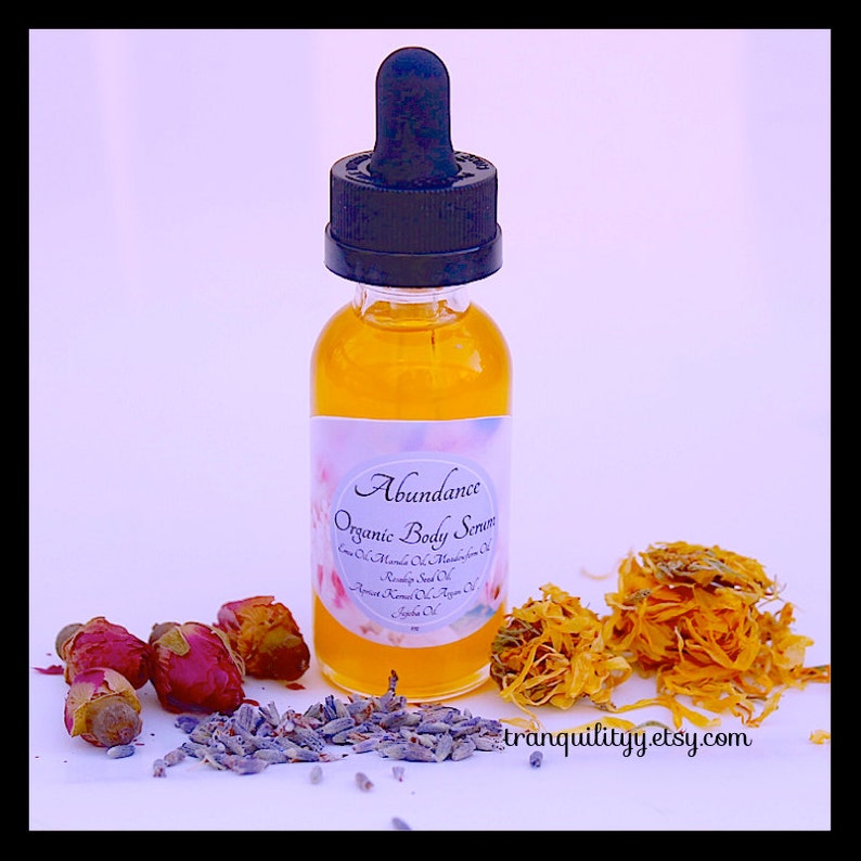 Pu&ograve; includere: Una bottiglia di vetro trasparente di siero corpo biologico con contagocce nero, etichettata "Abundance". Il siero &egrave; circondato da boccioli di rosa secchi, lavanda e petali di calendula. Su sfondo bianco.