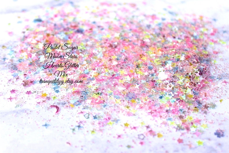 May include: Pastel pink, blue, and yellow glitter in the shape of stars and hearts. The glitter is scattered on a white surface. The text "Pastel Sugar Moon Stars Hearts Glitter Mix tranquilityy.etsy.com" is visible in the image.