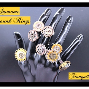May include: A hand model wearing a set of six steampunk rings featuring intricate gear designs in gold, silver, and bronze tones. The rings are displayed on a black background with the text "Awesome Steampunk Rings" and "Tranquilityy" in yellow.