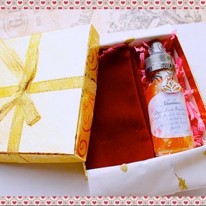 Pu&ograve; includere: Confezione regalo bianca con fiocco dorato, contenente un flacone di siero biologico per viso e corpo "Abundance". La bottiglia &egrave; circondata da carta rosa e un sacchetto di velluto rosso. La scatola ha un motivo floreale dorato.