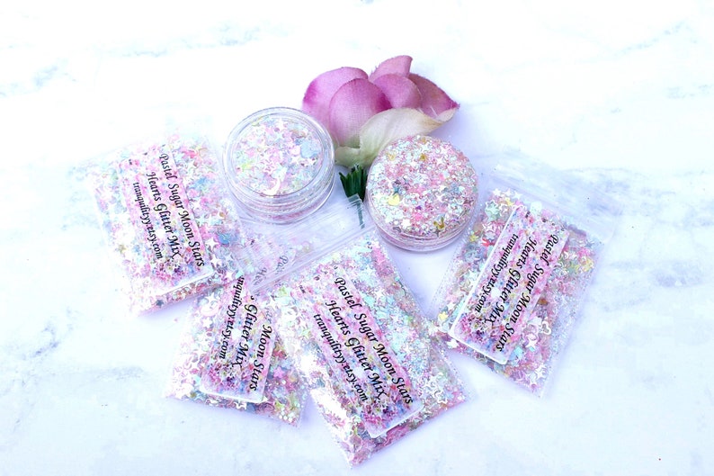 May include: Pastel pink, blue, and white glitter mix in small clear plastic bags with the text "Pastel Sugar Moon Stars Hearts Glitter Mix tranquilityy.etsy.com".