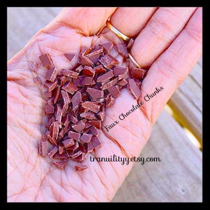 Puede incluir: Primer plano de una mano que sostiene trozos de chocolate falso. Los trozos son de color marrón rojizo oscuro y tienen forma irregular. El texto "Faux Chocolate Chunks" y "tranquilityy.etsy.com" son visibles.