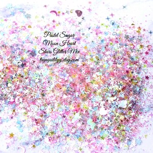 May include: Pastel pink, blue, and white glitter mix with stars, hearts, and moons. The glitter is scattered on a white surface. The text "Pastel Sugar Moon Heart Stars Glitter Mix tranquilityyy.etsy.com" is printed on the image.