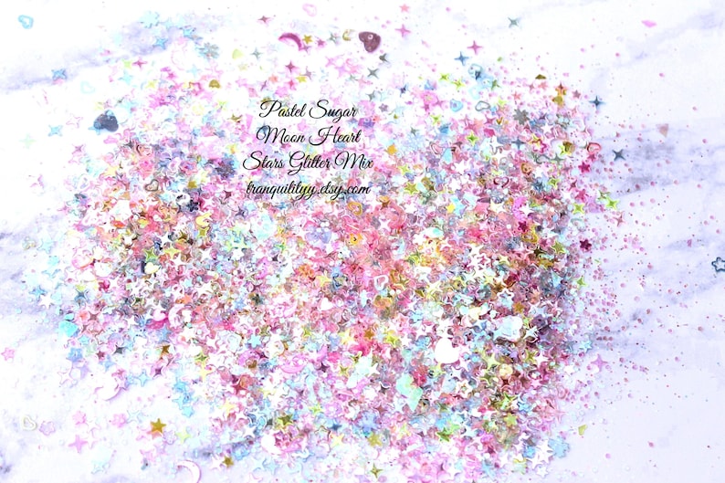 May include: Pastel pink, blue, and white glitter mix with stars, hearts, and moons. The glitter is scattered on a white surface. The text "Pastel Sugar Moon Heart Stars Glitter Mix tranquilityyy.etsy.com" is printed on the image.