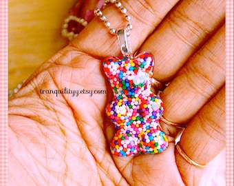 May include: A silver chain necklace with a gummy bear charm. The gummy bear is clear and filled with colorful sprinkles.